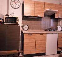Prevádzková budova-AUTOSERVIS na predaj vo Veľkých Úľanoch - Kuchyňa s dreveným dekorom, mikrovlnkou, dvoma hodinami a spotrebičmi na linke.