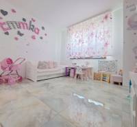 Neodolateľná ponuka! 4-izbová novostavba Galanta-Kolónia za super cenu - Detská izba v rodinnom dome s dekoráciami, kočíkom a písacími stolíkmi. Podlaha má drevený dekor.