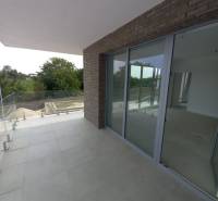 SKOLAUDOVANÉ! Novostavba 2,3 izbových bytov a nebytových priestorov - Balkón 2-izbového bytu v Galante s dlažbou a presklením, obklopený zeleňou.