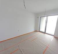 SKOLAUDOVANÉ! Posledné voľné obchodné priestory na predaj v novostavbe - Obchodné priestory s veľkým oknom, biela maľovka, podlaha s dreveným dekorom prikrytá fóliou.