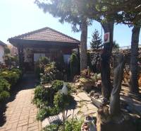 Predaj RD v Šali s bazénom - Rodinný dom v Šali s krásnou záhradkou, sochami a stromami v pozadí.