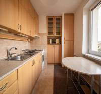 Rezervované: Na predaj pekný 2-izbový byt v centre mesta Poprad - Kuchyňa v 2-izbovom byte s podlahou s dreveným dekorom, svetlým nábytkom a stolom pri okne.