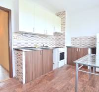 BAKOŠOVA, 1-i byt, 43 m2 – nerušený VÝHĽAD NA KARPATY - Kuchyňa v 1-izbovom byte s podlahou s dreveným dekorom, biele skrinky, sklenený stôl.