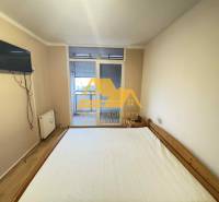 Prenajmem 3 izbový byt na sídlisku Juh v Nových Zámkoch - Spálňa v 3-izbovom byte s posteľou, televízorom na stene a vstupom na balkón.