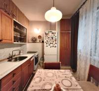 NA PREDAJ • 3i BYT S LOGGIOU • KALINČIAKOVA ULICA, SENICA - Kuchyňa v 3-izbovom byte s drevenými skrinkami a chladničkou, ozdobená záclonami.