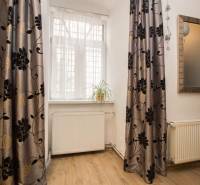 Centrum Košíc - 2-izb.tehlový byt s parkovaním vo dvore - Izba v 2-izbovom byte s podlahou s dreveným dekorom, závesmi a kvetinou na parapete.