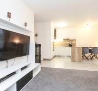 3i byt + záhradka 94m2 + parking, Vinohrady, Trenčín - Obývacia izba v 3-izbovom byte s televízorom, koberec a kuchynský kút so stoličkami.