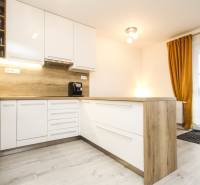3i byt + záhradka 94m2 + parking, Vinohrady, Trenčín - Kuchyňa v 3-izbovom byte s bielymi skrinkami, drevenou pracovnou doskou a závesmi.