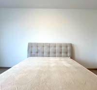 Súčasný 2-izbový byt v novostavbe – Matadorka  - Matrac s čalúneným čelom na posteli v dvojgarsónke, s podlahou s dreveným dekorom.