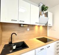 Súčasný 2-izbový byt v novostavbe – Matadorka  - Kuchynská linka v Dvojgarsónke s bielymi skrinkami a podlahou s dreveným dekorom.