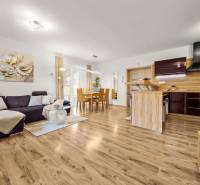 MODERNÝ 5-IZBOVÝ RODINNÝ DOM V ČUNOVE: 180m2 KOMFORTU A TICHA - Obývacia izba a kuchyňa v rodinnom dome s podlahou s dreveným dekorom, pohodlný gauč.