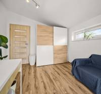 MODERNÝ 5-IZBOVÝ RODINNÝ DOM V ČUNOVE: 180m2 KOMFORTU A TICHA - Izba v rodinnom dome s podlahou s dreveným dekorom, skriňou a pohovkou.