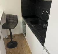 REZERVOVANÉ! Nadštandardný 1-izbový byt, ul. 1. mája, Vráble - Kuchyňa v 1-izbovom byte s čiernou doskou a podlahou s dreveným dekorom.