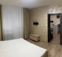 REZERVOVANÉ! Nadštandardný 1-izbový byt, ul. 1. mája, Vráble - Spálňový priestor s posteľou, závesmi a podlahou s dreveným dekorom v 1-izbovom byte.