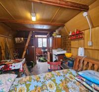 NA PREDAJ - ÚTULNÁ DREVENÁ CHATKA V DUBNICI NAD VÁHOM - Interiér chaty s dreveným dekorom, nábytkom a kuchynskými potrebami.