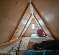 NA PREDAJ - ÚTULNÁ DREVENÁ CHATKA V DUBNICI NAD VÁHOM - Podkrovie chaty s matracom a stoličkou, drevený dekor, svetlé steny.