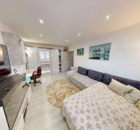 (56 m²) PRÍJEMNÝ 2i BYT NA SÍDLISKU TARČA - Obývačka v 2-izbovom byte s kobercami, sedačkou a podlahou s dreveným dekorom.