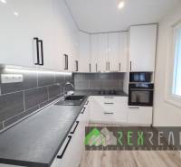 Predaj 3 izbového bytu s loggiou, Lučenec, Rúbanisko III.  - Kuchyňa v 3-izbovom byte s bielymi skrinkami a podlahou s dreveným dekorom.