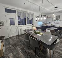 RODINNÝ DOM, HERNÁDKAK, MAĎARSKO - Jedálenský priestor s kamenným stolom, sivými stoličkami a závesnými svetlami v rodinnom dome.