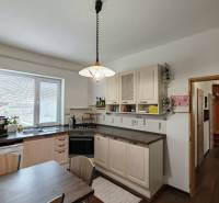 Na predaj rodinný dom v Trnovci nad Váhom - Kuchyňa v rodinnom dome so svetlom, drezom, umývačkou a stolom, podlaha s dreveným dekorom.