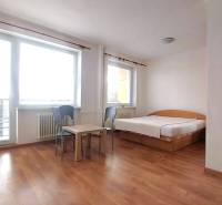 Slnečný 1 izb. byt Piešťany, praktická poloha, kúpou voľný - Jednoizbový byt s posteľou, stolíkom, stoličkami a podlahou s dreveným dekorom.