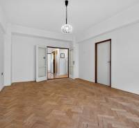I PREDAJ Priestranný 3-izb. byt v centre Krížna/Blumentálska - Prázdna izba v 3-izbovom byte s podlahou s dreveným dekorom, bielymi stenami a lustrom.