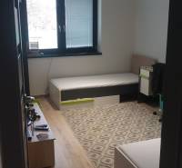 Predaj 4-izbového rodinného domu s veľkou záhradou v Semerove - Izba v rodinnom dome s podlahou s dreveným dekorom, postele, koberček a okno.