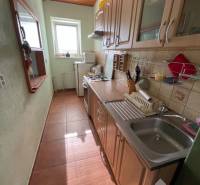 Veľký rodinný dom Podhradie  - Úzka kuchyňa v rodinnom dome s oknom a spotrebičmi, dominuje drevený dekor skriniek.