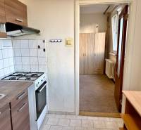 REZERVOVANÉ Na predaj 1 izbový byt, Bratislava, Dúbravka, Drobného - Kuchyňa s bielymi obkladačkami, sporákom, skrinkami a pohľad do predsiene v 1-izbovom byte.