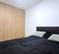 Moderný, rekonštruovaný 3i byt, pivnica, Jašíkova ul., Ružinov - Pošeň - Spálňa v 3-izbovom byte s bielymi stenami a vstavanou skriňou s dreveným dekorom.