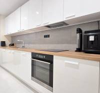 Moderný, rekonštruovaný 3i byt, pivnica, Jašíkova ul., Ružinov - Pošeň - Kuchyňa v 3-izbovom byte s bielymi skrinkami, spotrebičmi a pultom s dreveným dekorom.