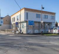 NA PREDAJ polyfunkčná budova v centre obce Veľké Leváre - Budova vo Veľkých Levároch, pri ceste, s parkovaným autom a dopravnými značkami.