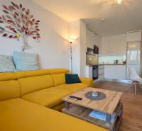 ŠTÝLOVÝ 3,5-IZBOVÝ BYT S NÁBYTKOM NA MIERU, A. HLINKU, ZVOLEN - Svetlá kuchyňa s podlahou s dreveným dekorom a žltou sedačkou v 3-izbovom byte.