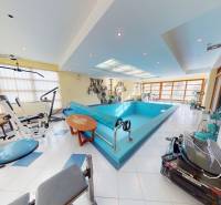 Veľkometrážny dom s wellness, bazénom a investičným potenciálom - Interiér rodinného domu s bazénom a posilňovacími strojmi, svetlé priestory s veľkými oknami.