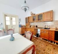 NA PREDAJ rodinný dom - Lehota nad Rimavicou - Kuchyňa v rodinnom dome s dreveným nábytkom, stolom a dekoračnou vázou.