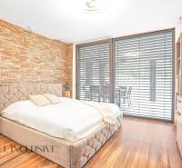 NA PREDAJ NADŠTANDARDNÁ 4-IZB. NOVOSTAVBA, DUN. KLÁTOV - Spálňa s kamennou stenou, pohodlnou posteľou a rozšíreným výhľadom cez okno v rodinnom dome.