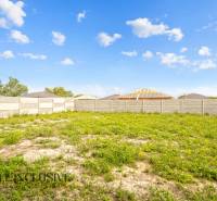 NA PREDAJ 4-IZBOVÁ NOVOSTAVBA, POVODA - Pozemok pri rodinných domoch na ulici Povoda, Dunajská Streda s plotom a trávou.