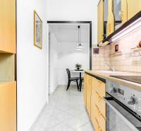 Zariadený 2-izbový byt, DVE NEPRIECHODNÉ IZBY, OC RETRO - Kuchyňa v 2-izbovom byte s krémovými skrinkami, jedálenským stolom a rastlinou.