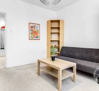 Zariadený 2-izbový byt, DVE NEPRIECHODNÉ IZBY, OC RETRO - Obývacia izba v 2-izbovom byte s pohovkou, stolíkom a poličkami, dekorované rastlinou a plagátom.