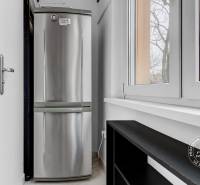 Zariadený 2-izbový byt, DVE NEPRIECHODNÉ IZBY, OC RETRO - Chladnička pri okne v 2-izbovom byte s výhľadom na stromy a budovy.