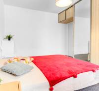 Zariadený 2-izbový byt, DVE NEPRIECHODNÉ IZBY, OC RETRO - Spálňa v 2-izbovom byte s posteľou, červenou prikrývkou a zrkadlovou skriňou.