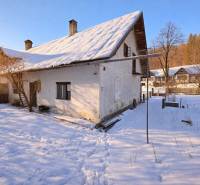 Predaj, rodinný dom Sliačany, Donovaly - Zasnežený rodinný dom v Donovaloch obklopený stromami a modrou oblohou.