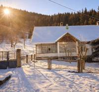 Predaj, rodinný dom Sliačany, Donovaly - Zasnežený rodinný dom v Donovaloch, obklopený stromami a zachytený pod zapadajúcim slnkom.
