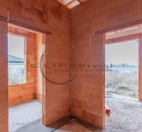 NA PREDAJ NOVOSTAVBA moderný 4-izbový rodinný dom v Malých Levároch - Nedokončená stavba rodinného domu so surovými tehlovými stenami a výhľadom von.