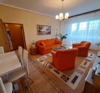 Pekný 2 izbový byt na Jadrovej ul. - Obývačka v 2-izbovom byte s oranžovým sedením, podlahou s dreveným dekorom a jedálenským stolom.