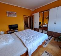 Pekný 2 izbový byt na Jadrovej ul. - Spálňa v 2-izbovom byte s posteľou, vstavanou skriňou a podlahou s dreveným dekorom.