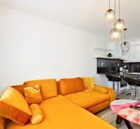 Mezonetový 3-izb. byt, Stará Ľubovňa, Popradská ulica - Obývačka 3-izbového bytu s oranžovou pohovkou, barovým pultom a dekoratívnymi svietidlami.