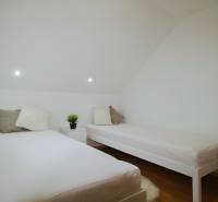 EXKLUZÍVNE / RODINNÝ DOM NA PREDAJ V OBCI SÚĽOV - Spálňa v rodinnom dome s dvomi posteľami a stolíkom, podlaha s dreveným dekorom.