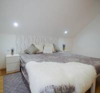 EXKLUZÍVNE / RODINNÝ DOM NA PREDAJ V OBCI SÚĽOV - Spálňa v rodinnom dome s posteľou, vankúšmi a nočnými stolíkmi na podlahe s dreveným dekorom.