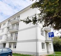 Na predaj 2 izb. byt s balkónom blízko centra, Chorvátsky Grob - Budova na Školskej ulici v Chorvátskom Grobe so zaparkovaným autom v pozadí.